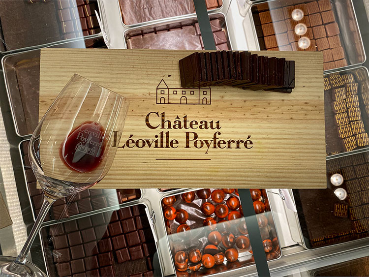 A wine glass laying flat on a Château Léoville-Poyferré board with Hasnaâ chocolats