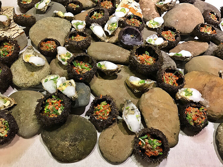 Raw oysters and sea urchin appetizers are arranged on a bed of rocks at Ciné Gourmand at La Cite du Vin