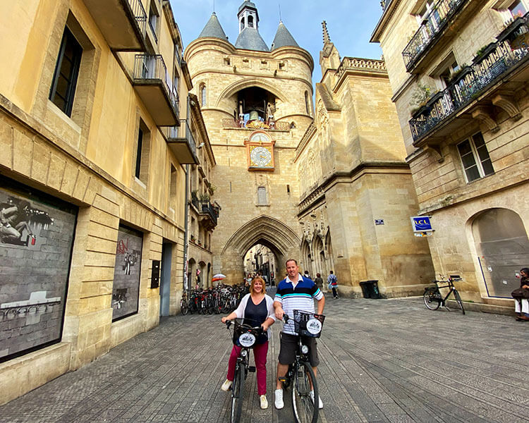 Jennifer and Tim pose on their bicycles in front of the Grosse Cloche in Bordeaux, France