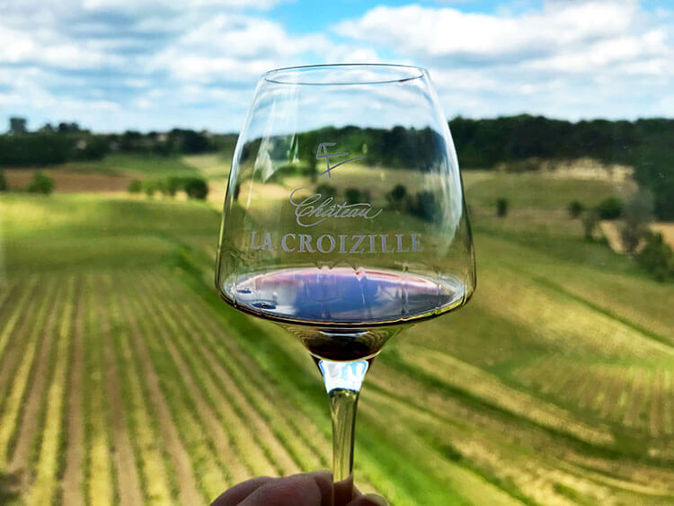 Holding up a glass of Château La Croizille to the view from the tasting room at Château La Croizille