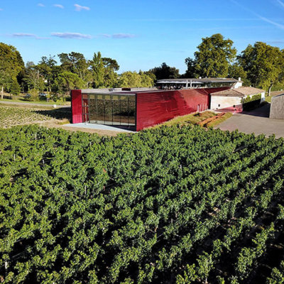 A drone shot of the vineyards and modern red winery of Château La Dominique