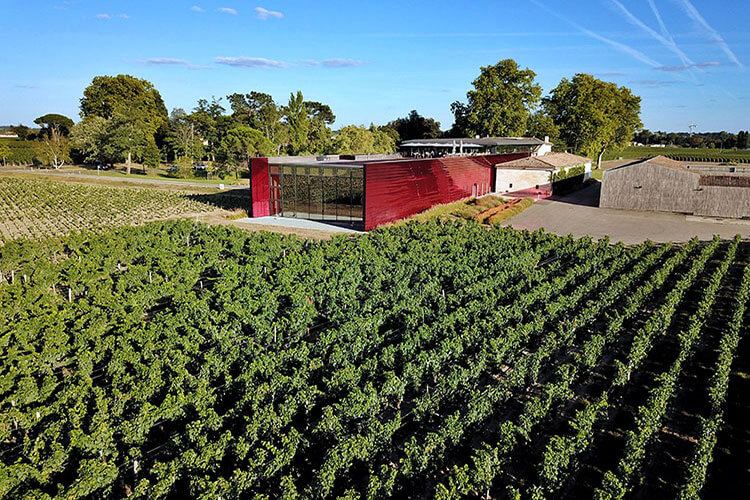 A drone shot of the vineyards and modern red winery of Château La Dominique