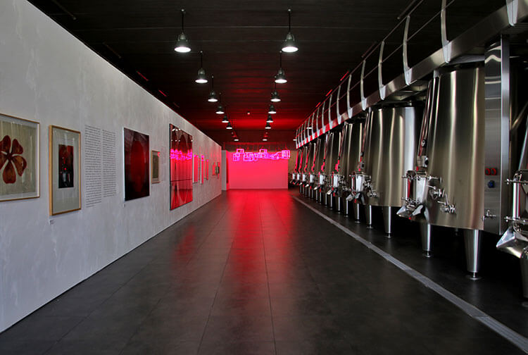 A temporary wall to house art works lines the left side of the vat room and the stainless steel vats are seem on the right