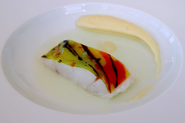 Sea bass filet topped with a red, yellow and green "skin" made of bergamot and harlequin at Restaurant Lalique at Chateau Lafaurie Peyraguey