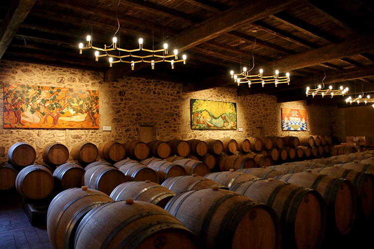 The barrel room is the old stable with wooden beams and artworks lining the stone walls at Chateau Sigalas Rabaud