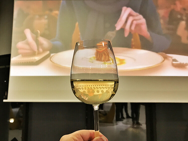 Jennifer holding a glass of white wine in front of the screen as scenes from Ratatouille play at Cine Gourmand