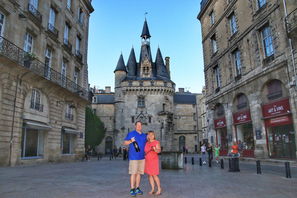Tim & Jennifer pose in front of the Port Cailhau gate in Bordeaux with Tim holding a Bordeaux magnum and Jennifer holding a giant antique key