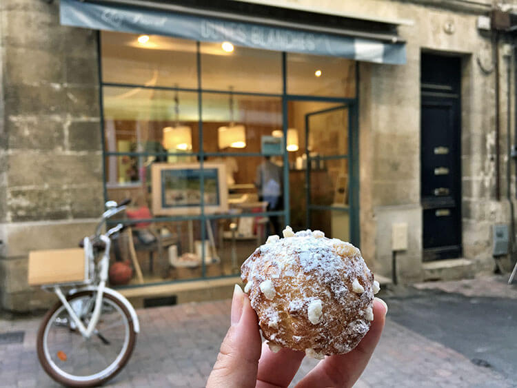 Holding up a single Dunes Blanches pastry in front of the Dunes Blanches Chez Pascal shop in Bordeaux