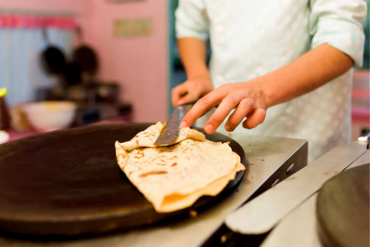 A chef uses a spatula to flip a crêpe