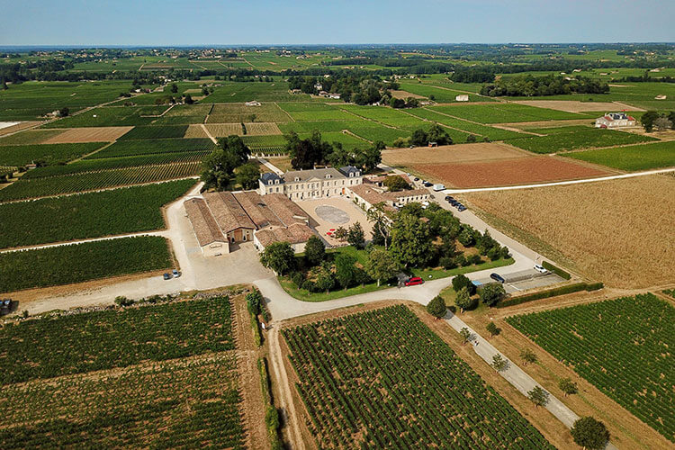 A drone aerial of the farmhouse complex of Chateau Soutard surrounded by vineyards in Saint-Émilion