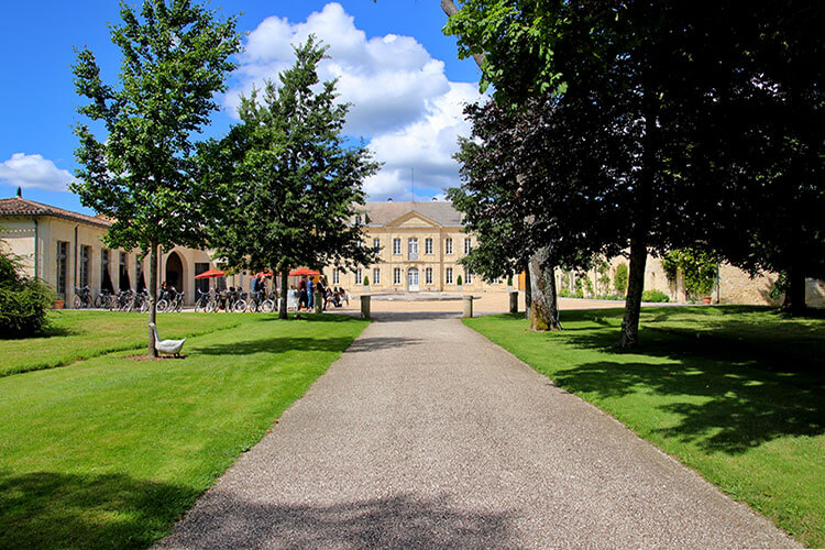 The main farm house of Château Soutard is framed by trees with umbrellas and tables set up as a wine bar in the courtyard