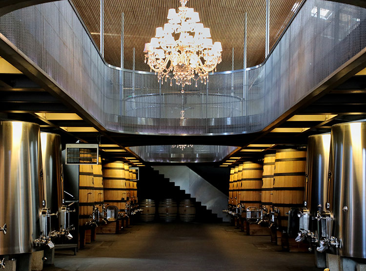 Stainless steel and wooden vats line the lower level of the vat room with an impressive and elegant chandelier hanging from ceiling at Château Soutard