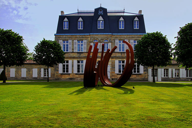 A metal sculpture sits on the lawn in front of the 19th century Château Malescasse