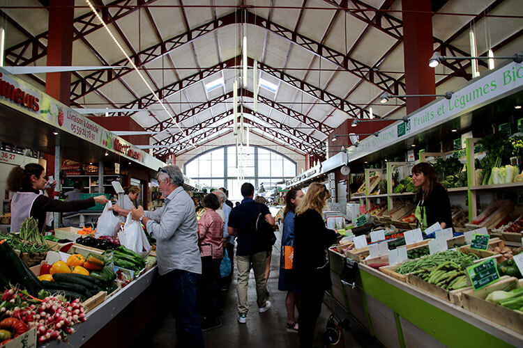 Looking down a row of Marche aux Halles de Biarritz where shoppers are buying from various produce stands