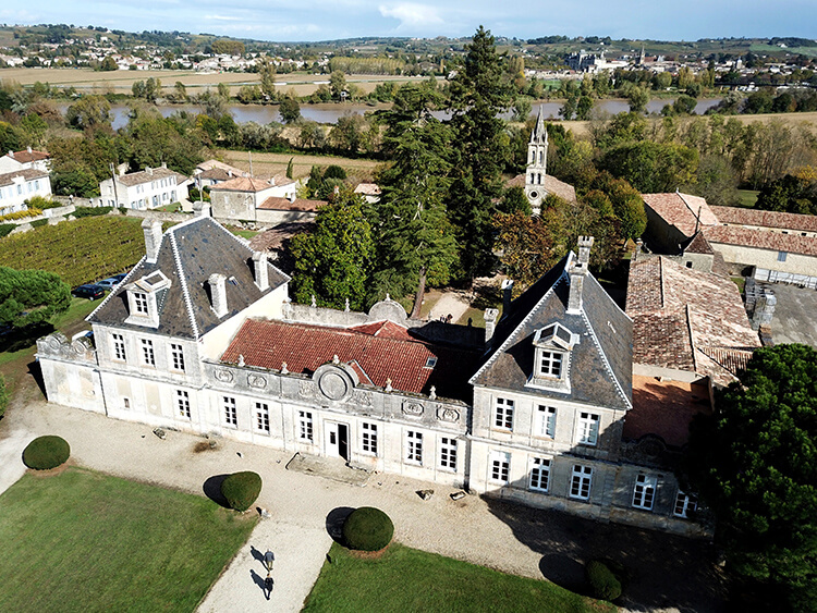 A drone aerial of Château de Cérons with the Ciron River visible behind, along with the towering magnolias and Giant Sequoia in the park