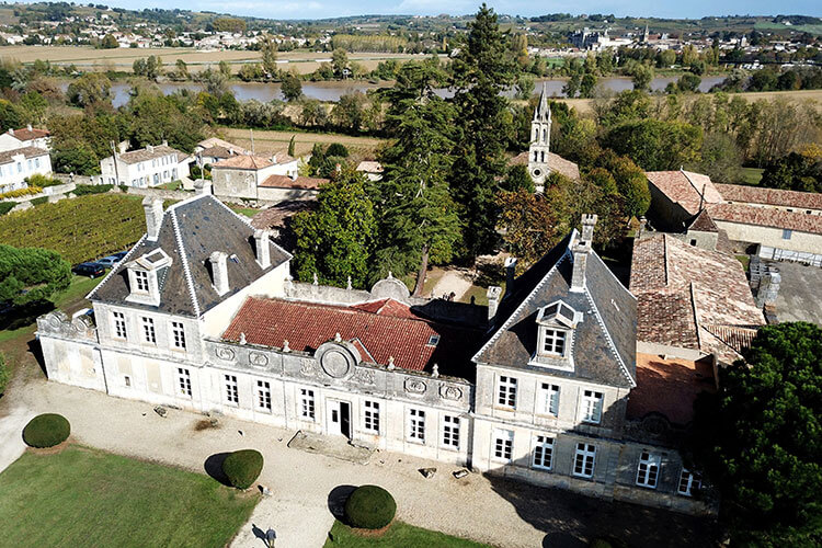 A drone aerial of Château de Cérons with the Ciron River visible behind, along with the towering magnolias and Giant Sequoia in the park