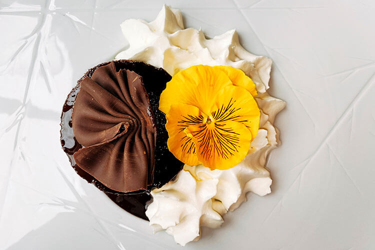 A chocolate fondant plated with chantilly cream at topped with an edible yellow flower at Atelier de Candale