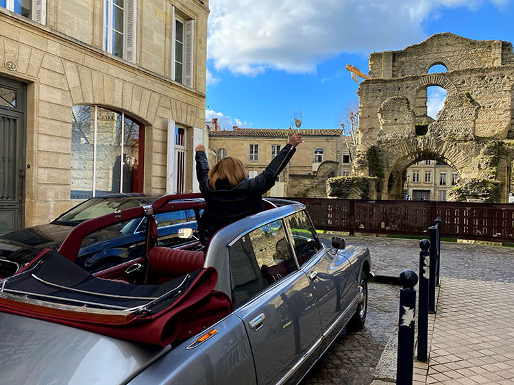 Jennifer looks at the Palais Gallien in Bordeaux while standing up in the open-top Citroën DS on a Bordeaux Classic Cars tour