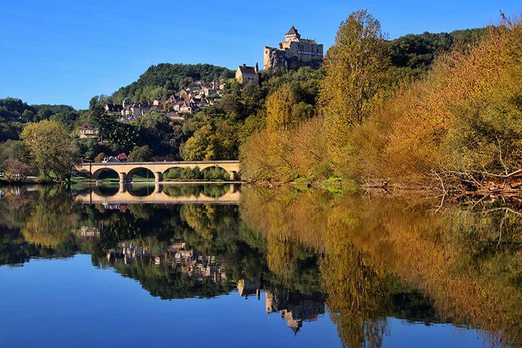 The village of Castelnaud and the Castelnaud Bridge reflect on the mirror-like Dordogne River