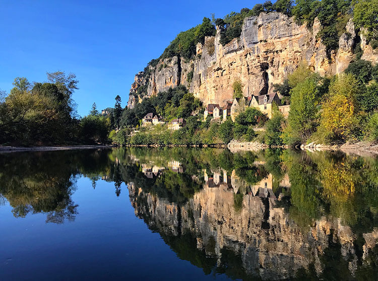 The village of Cénac-et-Saint-Julien and its limestone cliffs reflects on the mirror-like Dordogne River