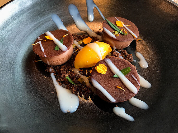 Chocolate mousse is topped with edible flowers and on a bed of chocolate crumble with mango sorbet in the center