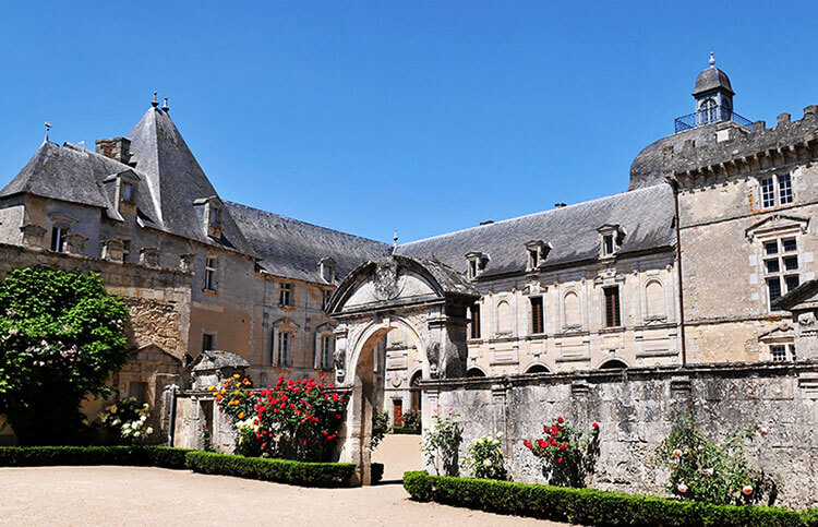 The entrance to the castle courtyard with red rose bushes lining the stone walls of Château de Vayres