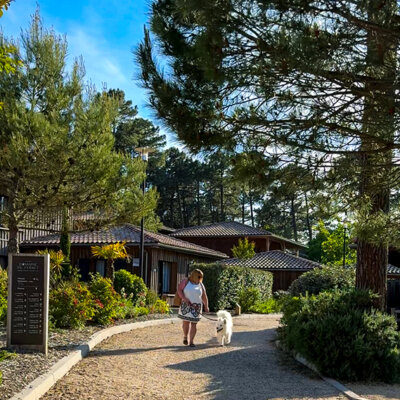 Jennifer and Coco walk on the path among the pine trees and lodges at Domaine du Ferret in Claouey, Lège-Cap-Ferret, France